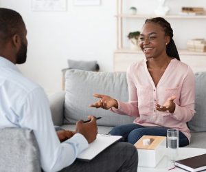 Happy african woman talking with psychologist at private therapy session, sharing her progress, sitting on couch and smiling, free space
